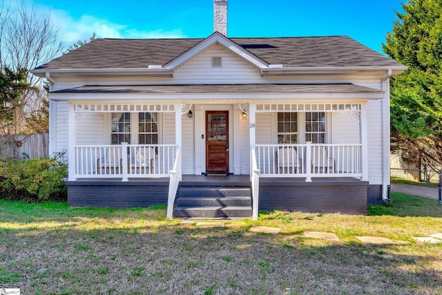 bungalow with a front yard, covered porch, roof with shingles, and fence