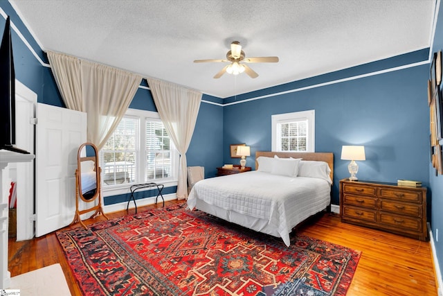 bedroom with a textured ceiling, ceiling fan, wood-type flooring, and baseboards