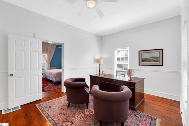 office area featuring dark wood-style flooring, visible vents, baseboards, a ceiling fan, and crown molding