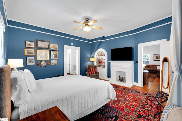 bedroom featuring a fireplace with raised hearth, ceiling fan, wood finished floors, and ensuite bathroom