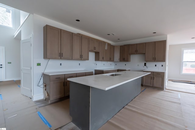 kitchen with a center island, light countertops, a sink, light wood-type flooring, and baseboards