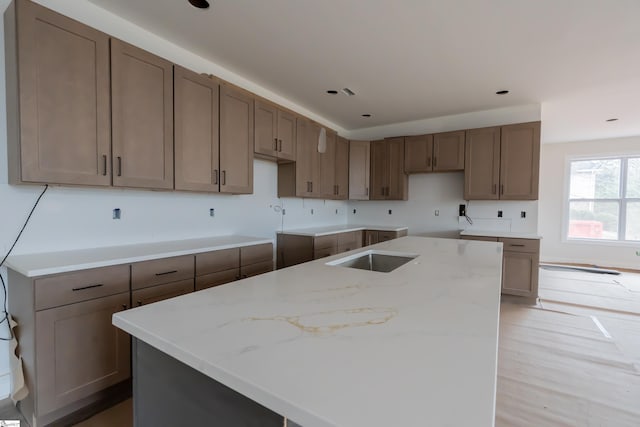 kitchen featuring a sink, light stone counters, a kitchen island, and light wood-style floors