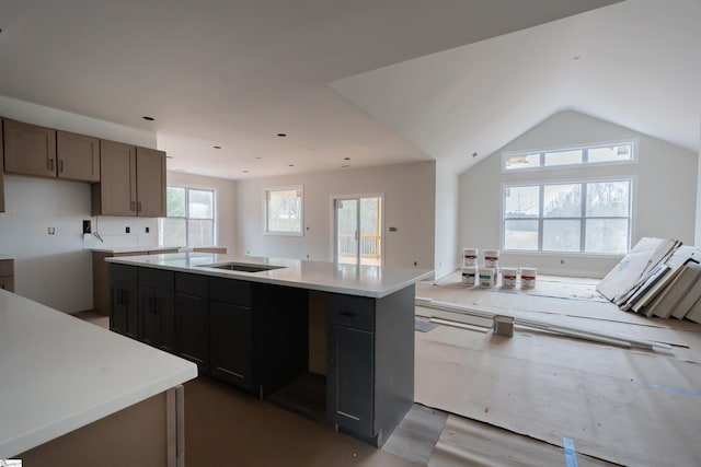 kitchen featuring lofted ceiling, light countertops, a sink, and a kitchen island with sink