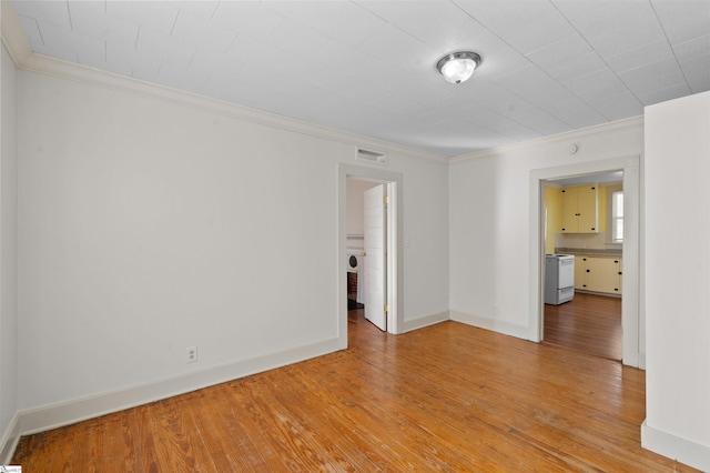 spare room with light wood-type flooring, baseboards, visible vents, and ornamental molding