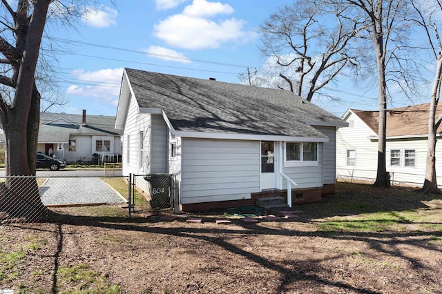 rear view of property featuring entry steps, driveway, fence, and roof with shingles