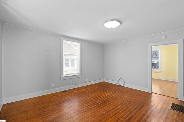 unfurnished room featuring hardwood / wood-style floors, visible vents, and baseboards