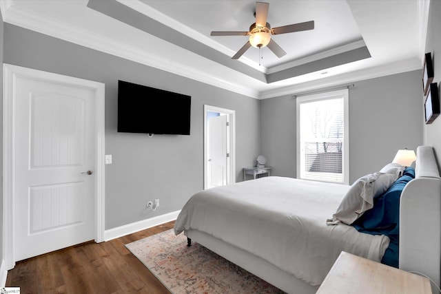 bedroom featuring a tray ceiling, dark wood-style flooring, crown molding, a ceiling fan, and baseboards