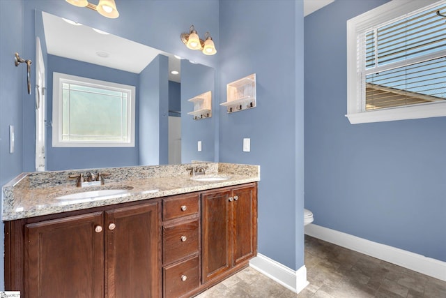 full bath featuring baseboards, a sink, toilet, and double vanity