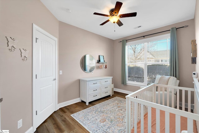 bedroom featuring baseboards, visible vents, dark wood finished floors, ceiling fan, and a nursery area