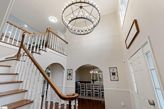 foyer with a chandelier, arched walkways, dark wood-style flooring, and a towering ceiling