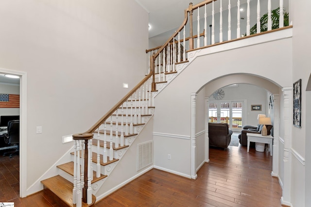 staircase featuring arched walkways, a high ceiling, hardwood / wood-style flooring, and visible vents