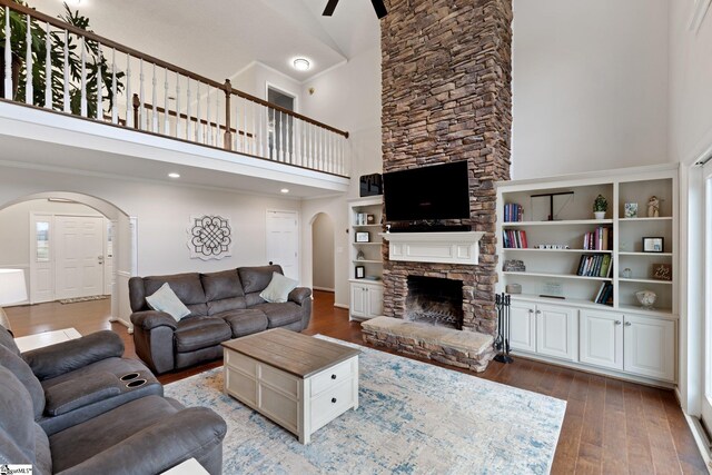 living room with a high ceiling, arched walkways, hardwood / wood-style floors, and a stone fireplace