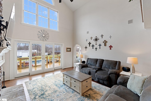 living area featuring arched walkways, ceiling fan, wood finished floors, visible vents, and french doors