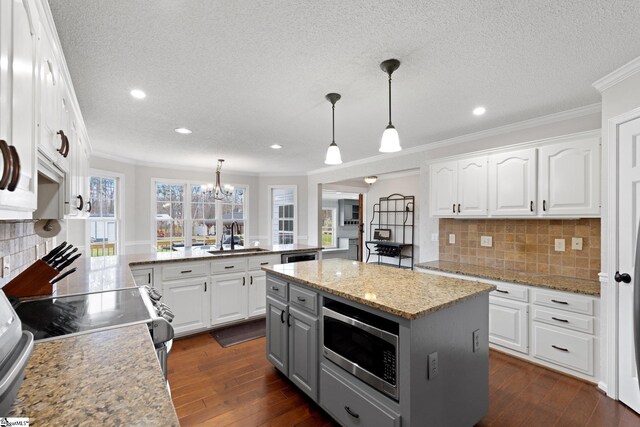 kitchen featuring white cabinets, a peninsula, light stone countertops, stainless steel appliances, and pendant lighting