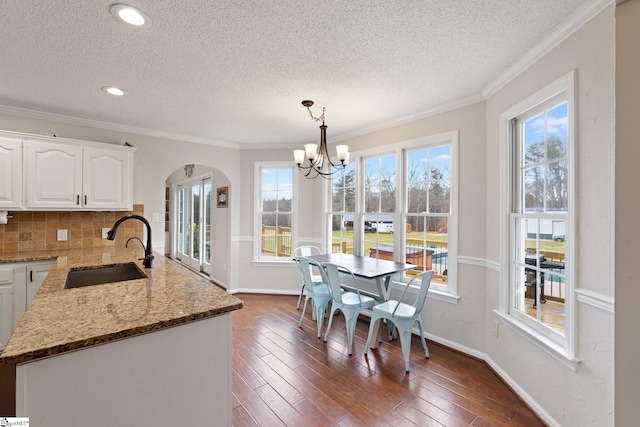 dining space featuring crown molding, arched walkways, dark wood finished floors, and an inviting chandelier