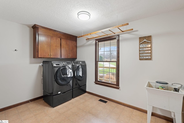 washroom featuring cabinet space, baseboards, visible vents, washing machine and clothes dryer, and a textured ceiling