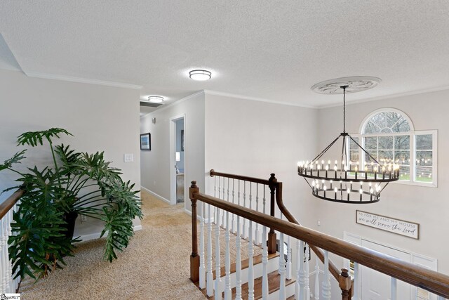 hall featuring a textured ceiling, carpet floors, an upstairs landing, baseboards, and ornamental molding