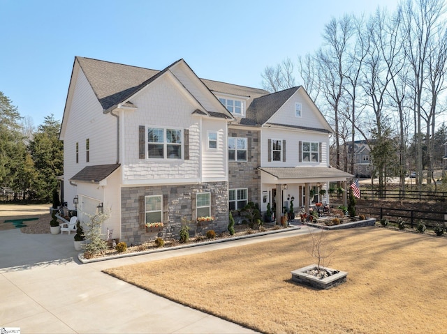 view of front facade featuring a porch, fence, a garage, stone siding, and driveway