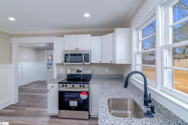 kitchen featuring white cabinetry, stainless steel appliances, a sink, and ornamental molding