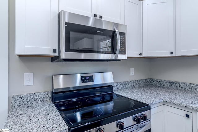 kitchen with stainless steel appliances, white cabinets, and light stone counters