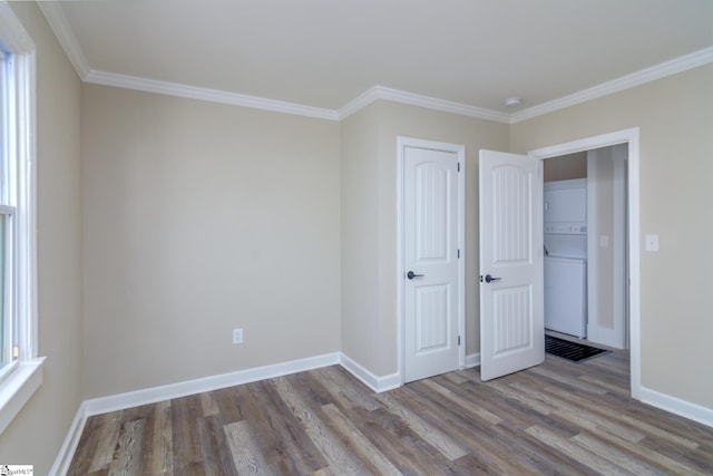 unfurnished bedroom with stacked washer / dryer, baseboards, light wood-style floors, ornamental molding, and multiple windows