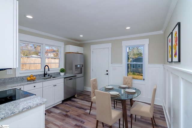 kitchen with light stone counters, stainless steel dishwasher, white cabinetry, a sink, and light wood-type flooring