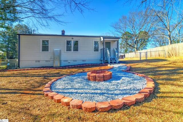 back of property featuring crawl space, fence, a fire pit, and a lawn