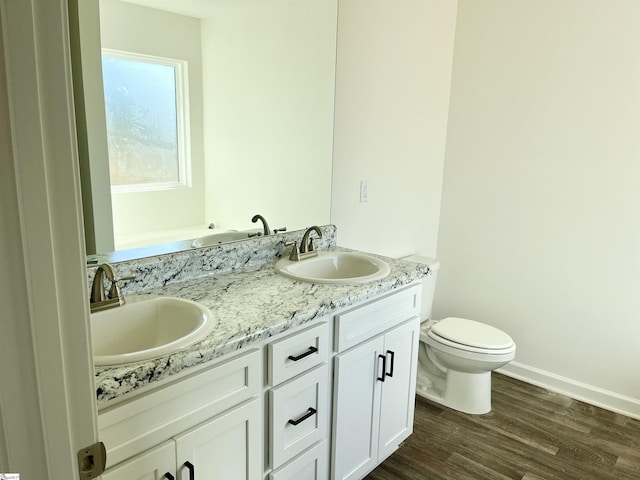 full bath with double vanity, wood finished floors, a sink, and toilet