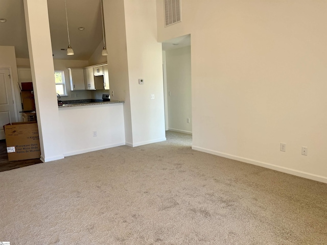 unfurnished living room with high vaulted ceiling, light colored carpet, visible vents, and baseboards