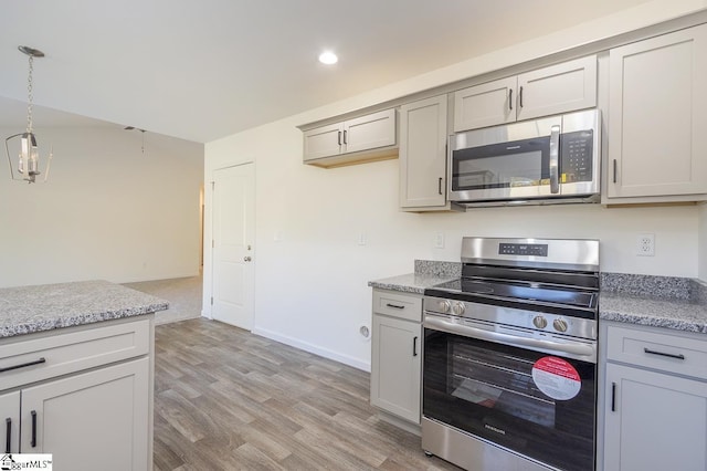 kitchen with light stone counters, gray cabinetry, stainless steel appliances, light wood finished floors, and decorative light fixtures