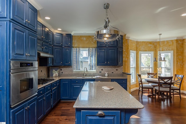 kitchen featuring appliances with stainless steel finishes, hanging light fixtures, under cabinet range hood, blue cabinetry, and a sink