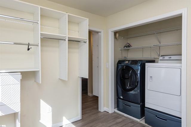 clothes washing area featuring laundry area, baseboards, wood finished floors, and washing machine and clothes dryer