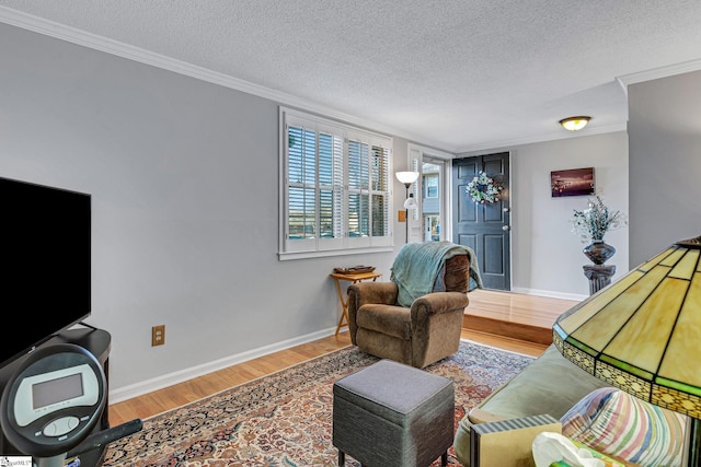 living room featuring a textured ceiling, ornamental molding, wood finished floors, and baseboards