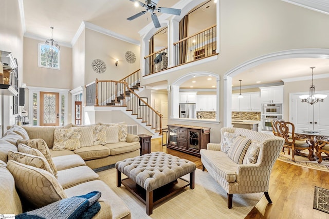 living room featuring ornate columns, ornamental molding, light wood-style floors, and ceiling fan with notable chandelier