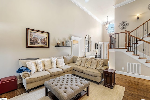 living room featuring visible vents, stairway, a towering ceiling, ornamental molding, and wood finished floors