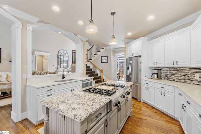 kitchen featuring a sink, white cabinets, appliances with stainless steel finishes, a center island, and decorative light fixtures