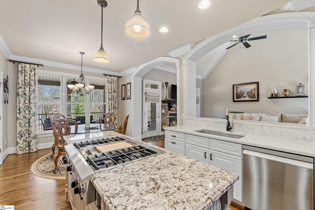 kitchen with arched walkways, pendant lighting, stainless steel dishwasher, white cabinetry, and a sink