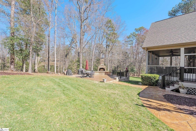 view of yard featuring a ceiling fan, an outdoor stone fireplace, and a patio area