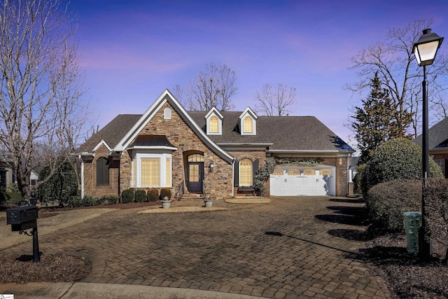 view of front facade featuring a garage, stone siding, roof with shingles, decorative driveway, and brick siding