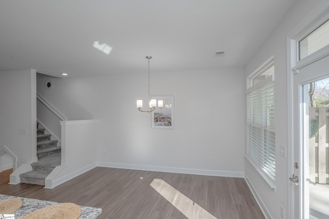 interior space with visible vents, stairway, wood finished floors, a chandelier, and baseboards