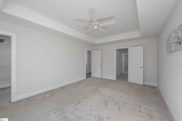 unfurnished bedroom with light carpet, baseboards, a closet, a tray ceiling, and a walk in closet