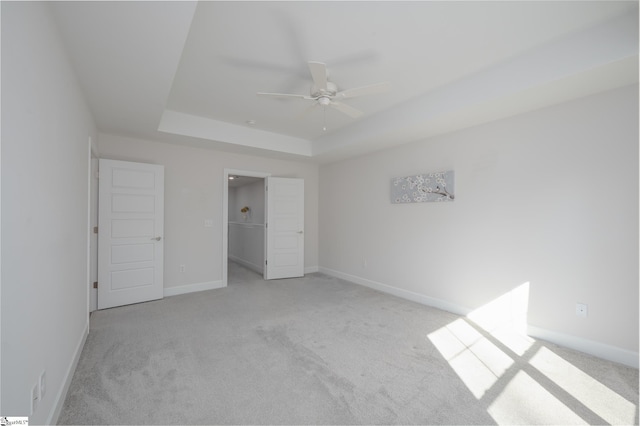 unfurnished bedroom with baseboards, a tray ceiling, a ceiling fan, and light colored carpet