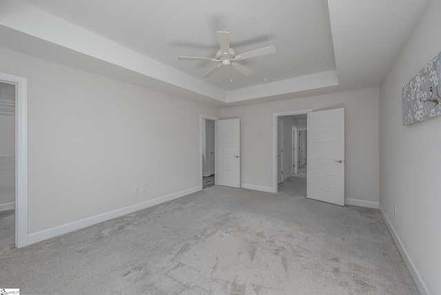 unfurnished bedroom with baseboards, a ceiling fan, light colored carpet, a spacious closet, and a tray ceiling