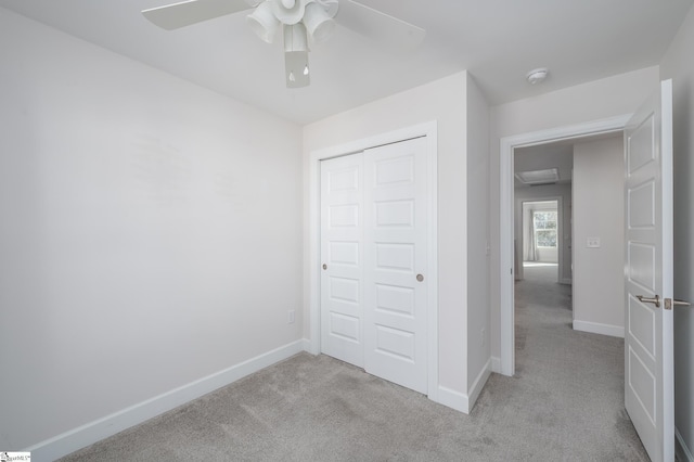 unfurnished bedroom featuring light carpet, ceiling fan, baseboards, and a closet