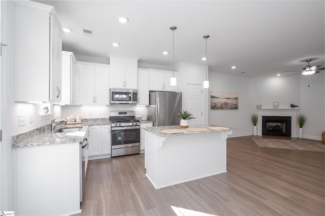 kitchen with stainless steel appliances, a kitchen island, white cabinetry, open floor plan, and decorative light fixtures