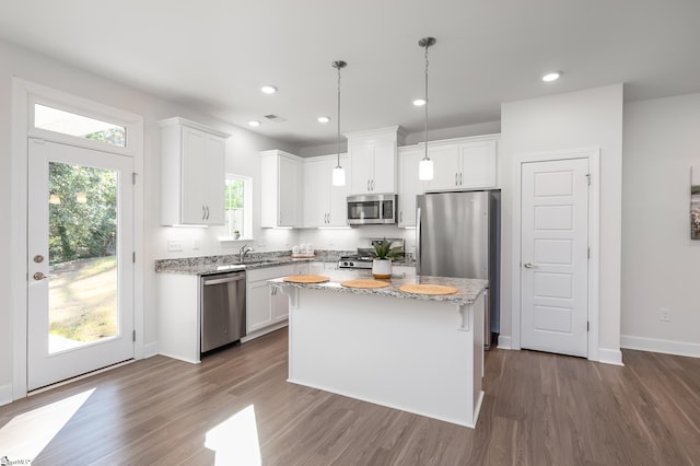 kitchen with a center island, hanging light fixtures, light stone countertops, stainless steel appliances, and white cabinetry