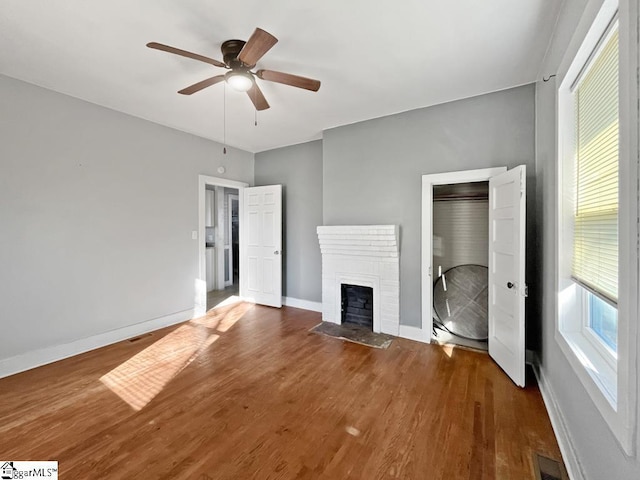 unfurnished living room with a brick fireplace, wood finished floors, visible vents, and baseboards