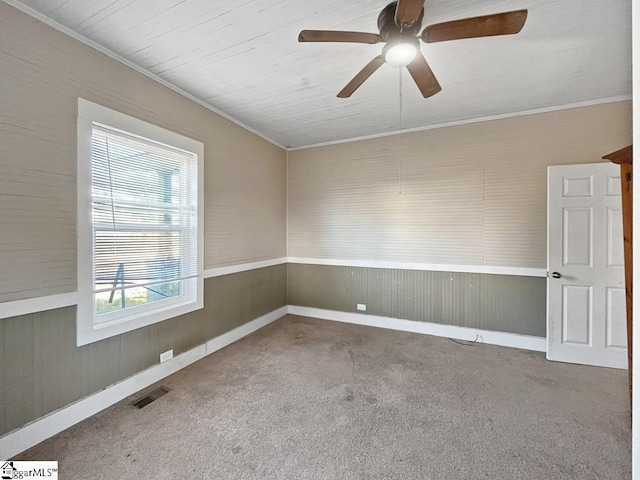 carpeted spare room with a ceiling fan, visible vents, and crown molding