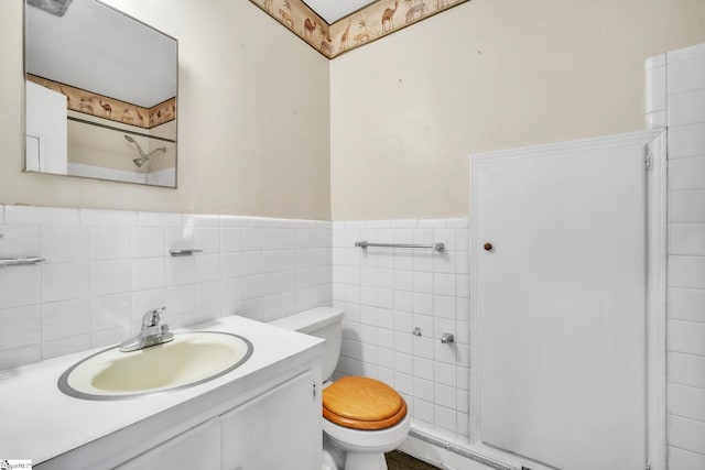 bathroom featuring toilet, a wainscoted wall, tile walls, and vanity