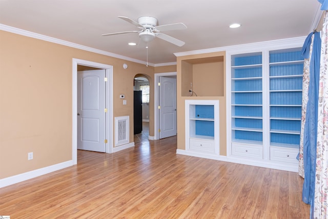 spare room featuring arched walkways, light wood-style flooring, visible vents, baseboards, and ornamental molding